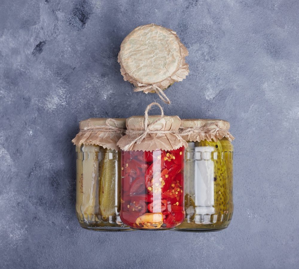 Pickled cucumbers and red peppers in glass jars on blue background Pepinos Encurtidos Y Pimientos Rojos En Frascos De Vidrio Sobre Fondo Azul Scaled